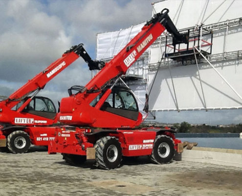 Telehandler mobile cranes holding up huge green screens on a film set