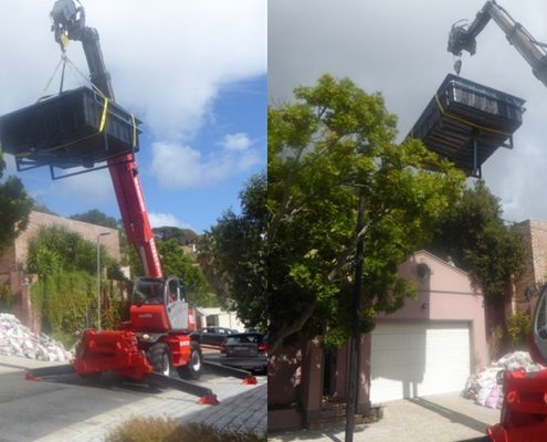 Mobile crane telehandler lifting a swimming pool over a wall