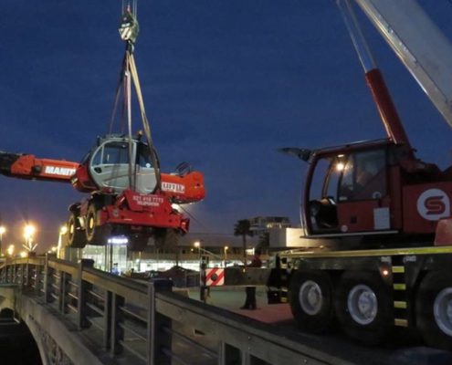 Using a Liebherr crane to lift a Manitou mobile crane into an empty canal.